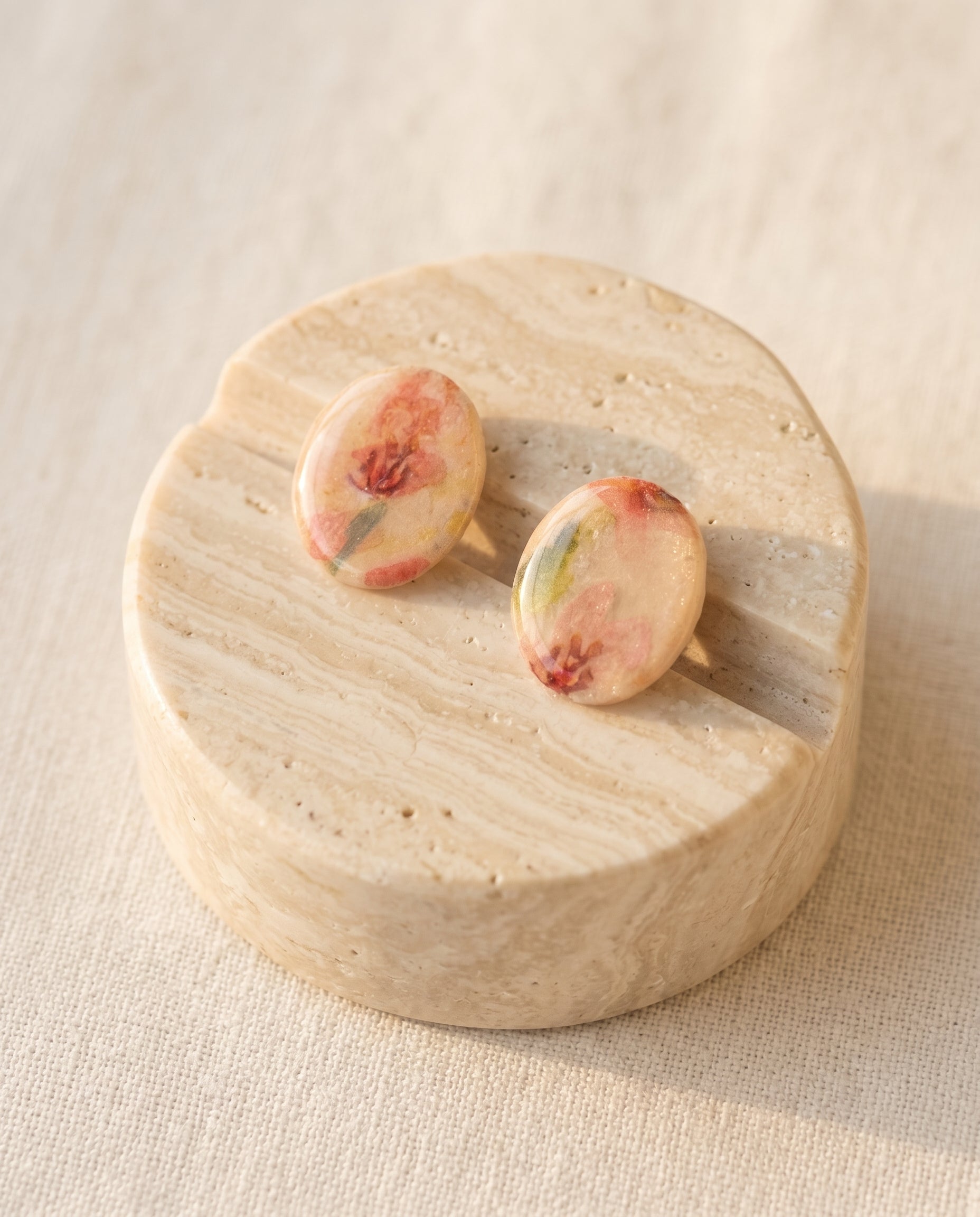Pendientes ovalados Kaiora Rose con ilustración floral en tonos rosados y carmines.