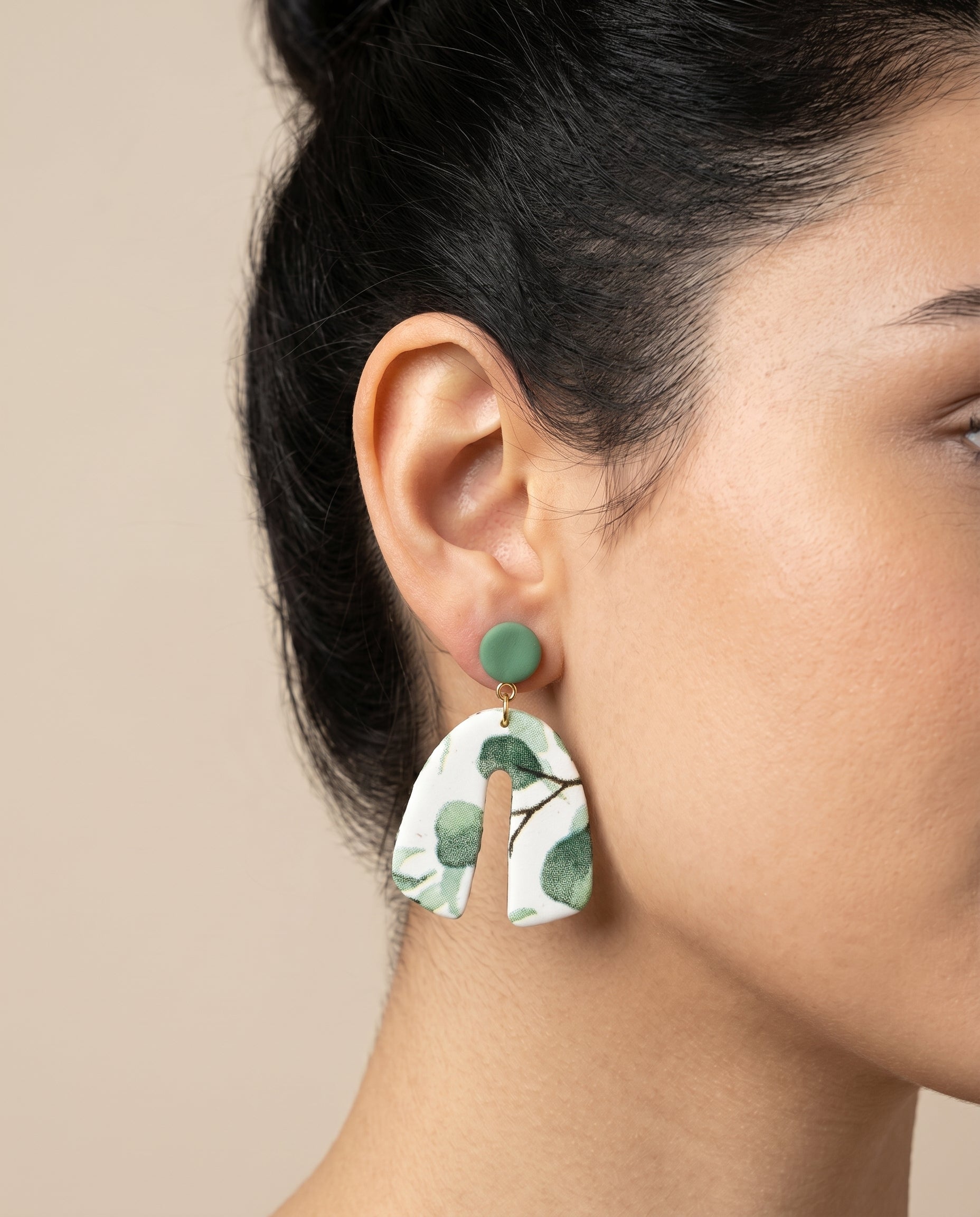 Pendientes Kaiora Bloom de arcilla polimérica blancos con estampado floral verde y forma de arco.