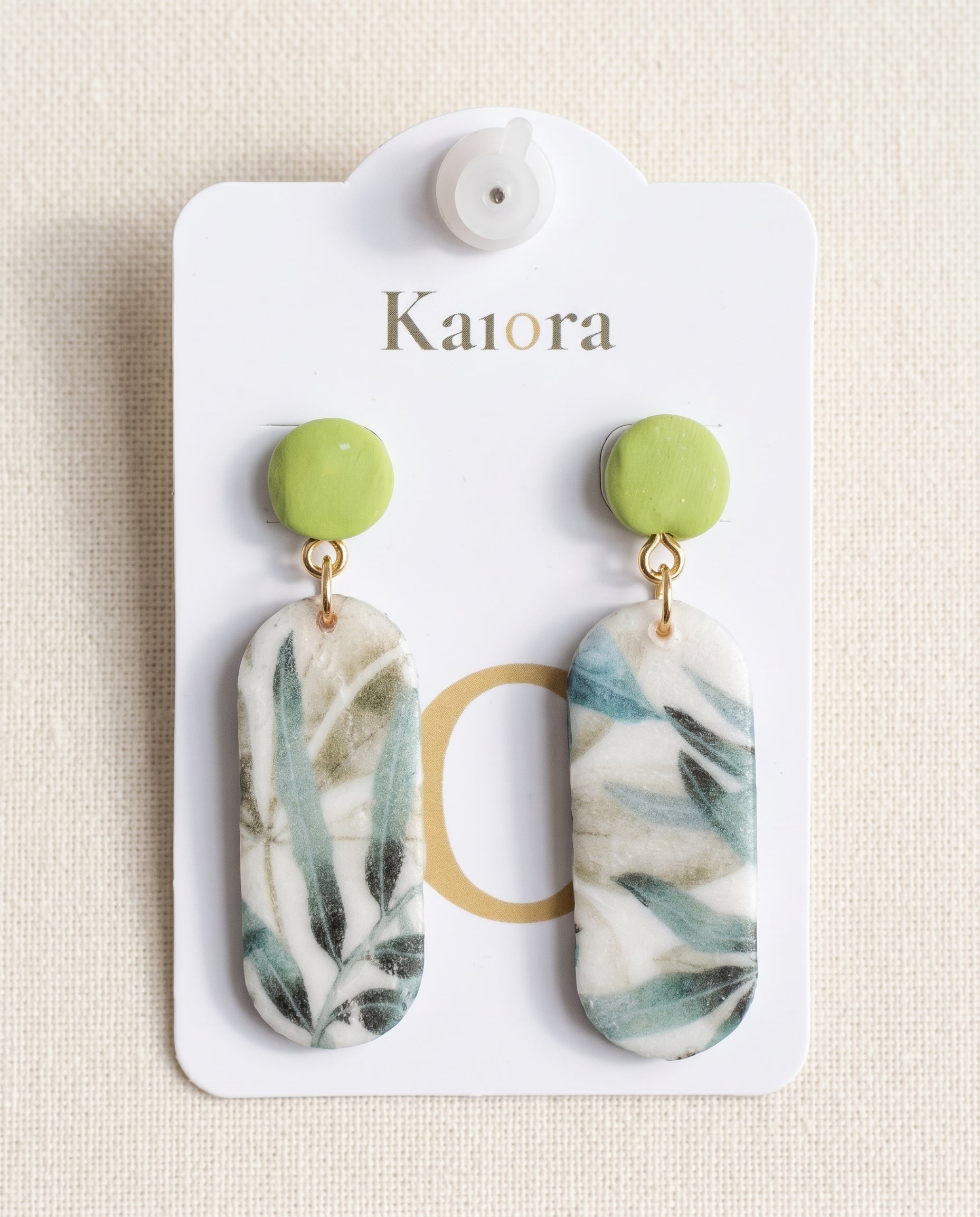 Pendientes Kaiora colgantes con hojas verdes y azules, base blanca y detalle superior verde.
