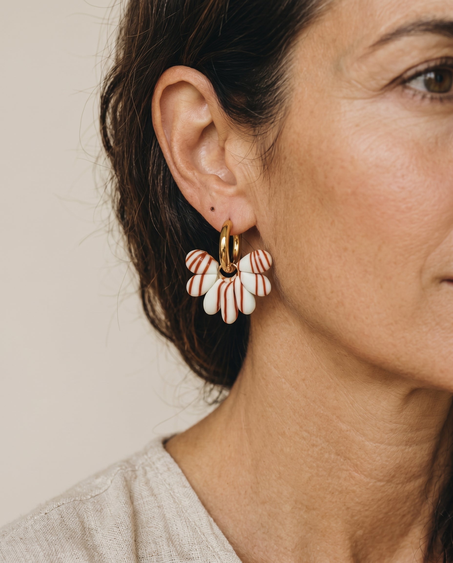 Pendientes Kaiora Dune Bloom dorados con pétalos crema y rayas tierra, diseño orgánico y femenino.