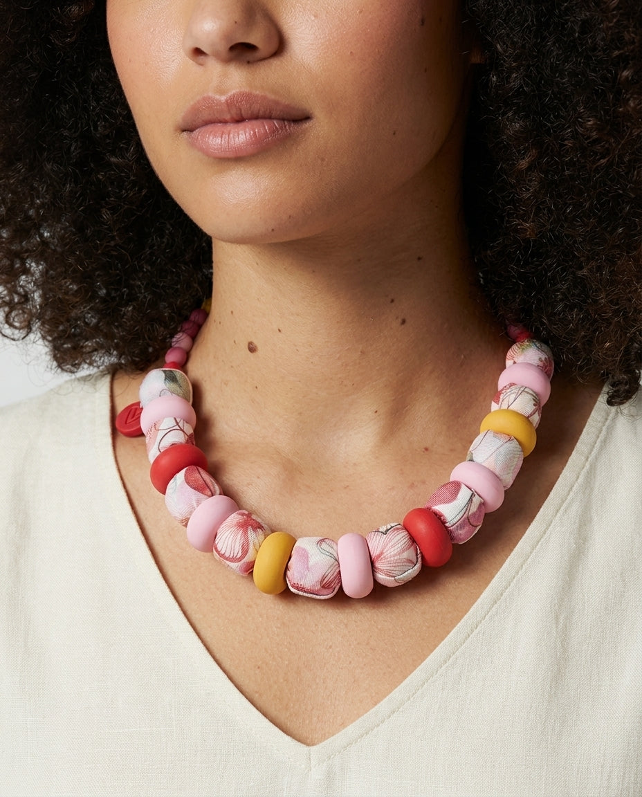 Collar Kaiora Lago de cuentas grandes textiles florales y lisas en tonos rosa, rojo y amarillo.